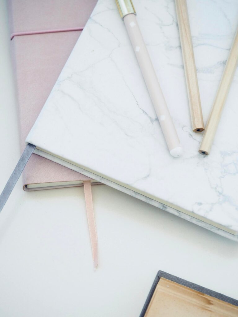 Stylish marble and pink notebooks paired with pens, creating an elegant and clean office desk setup.