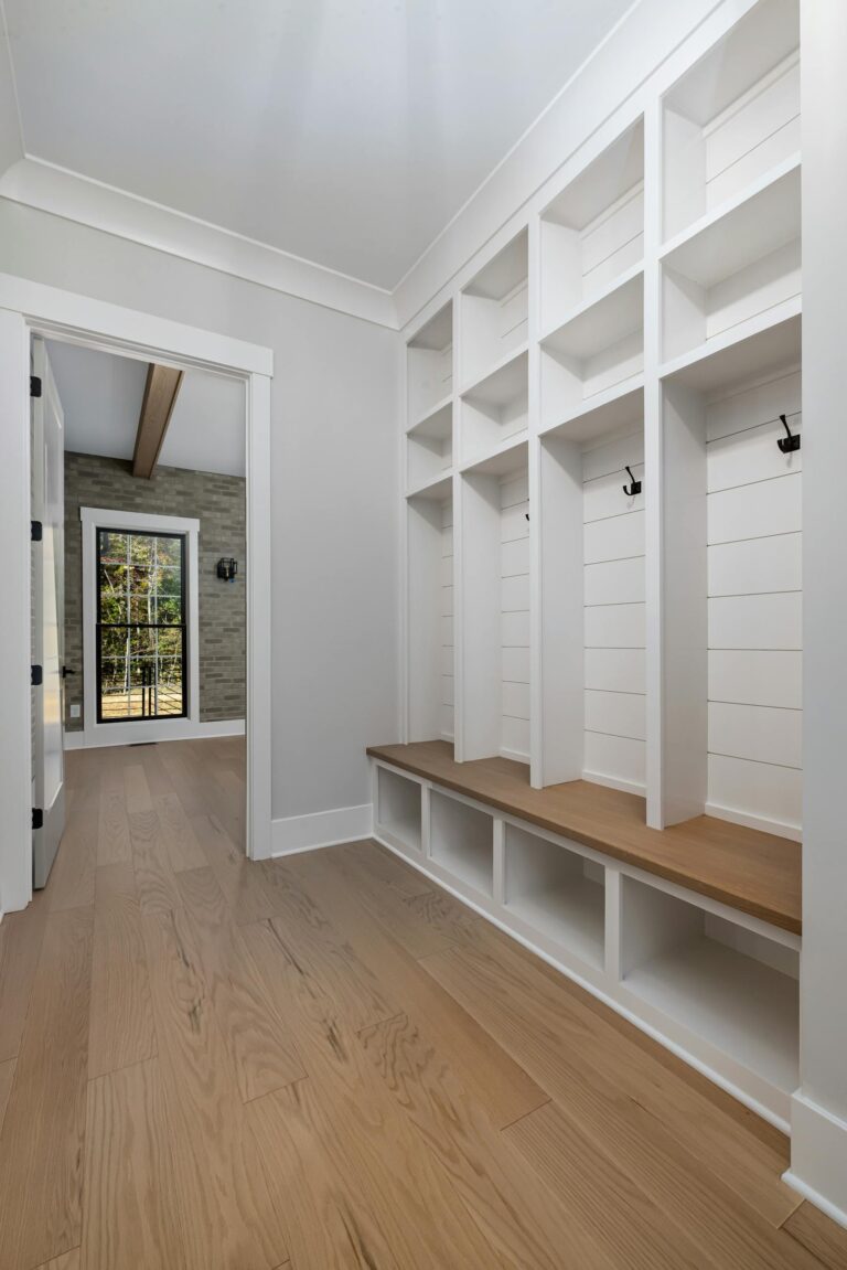 Spacious and stylish entryway featuring white built-in shelves and wooden floor.