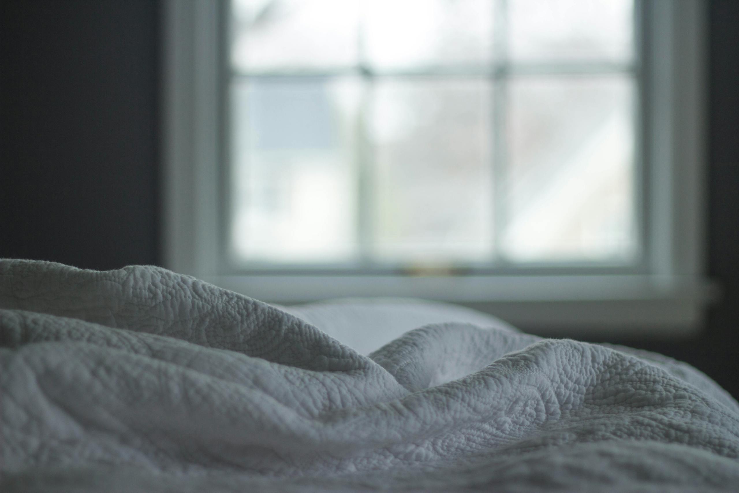 A tranquil bedroom view with a quilted blanket by the window softly lit by morning light, ideal for relaxation themes.