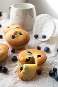 Freshly baked blueberry muffins with a coffee mug on a light background.