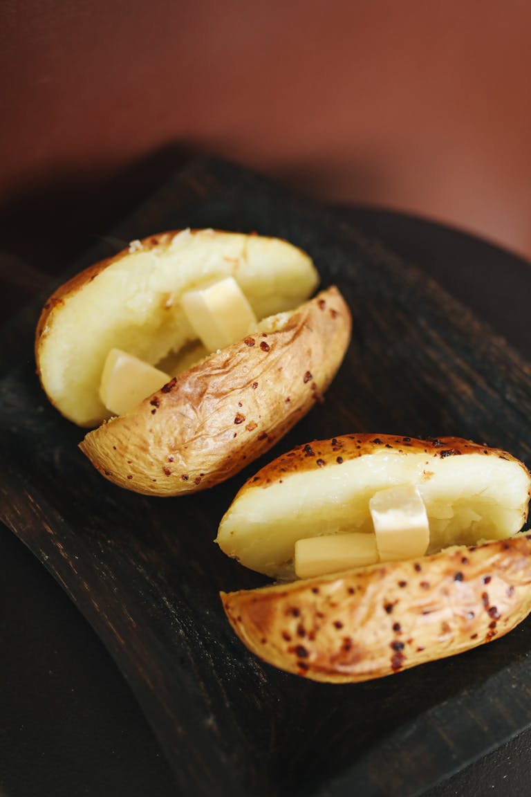 Three baked potato halves with butter on a rustic wooden tray, showcasing earthy texture and flavor.