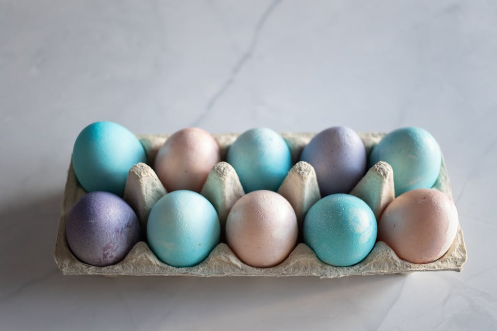 A beautifully arranged set of dyed Easter eggs in a carton on a marble surface.