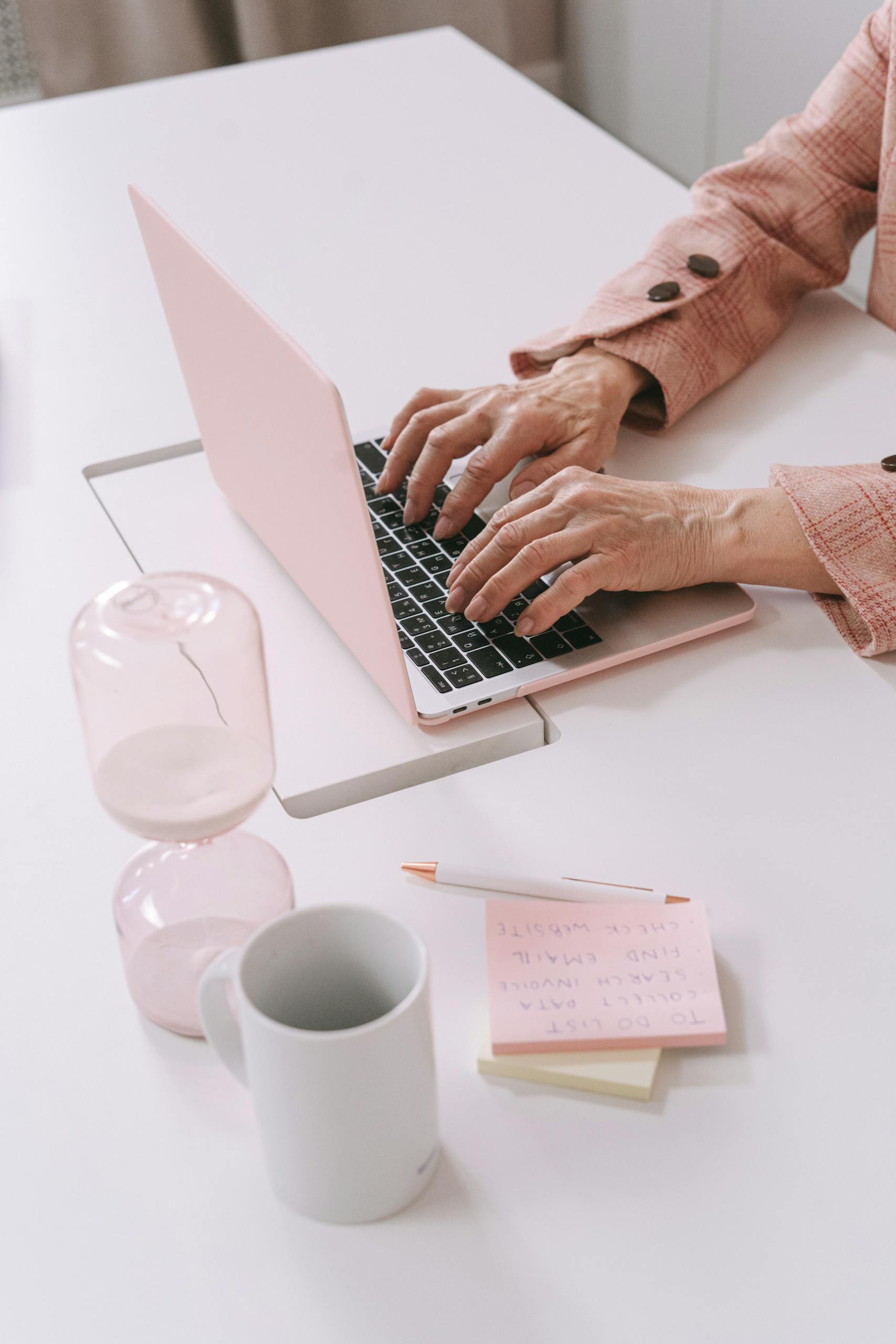 A woman working on a pink laptop in a stylish modern workspace with office supplies.