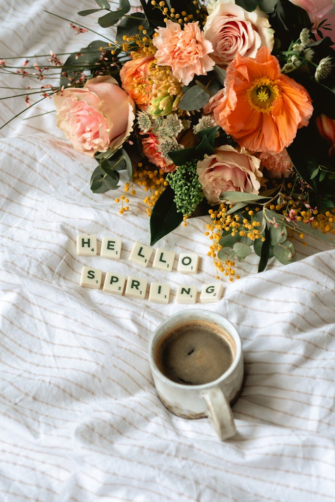 Charming spring flat lay with colorful flowers, coffee, and 'Hello Spring' tiles.