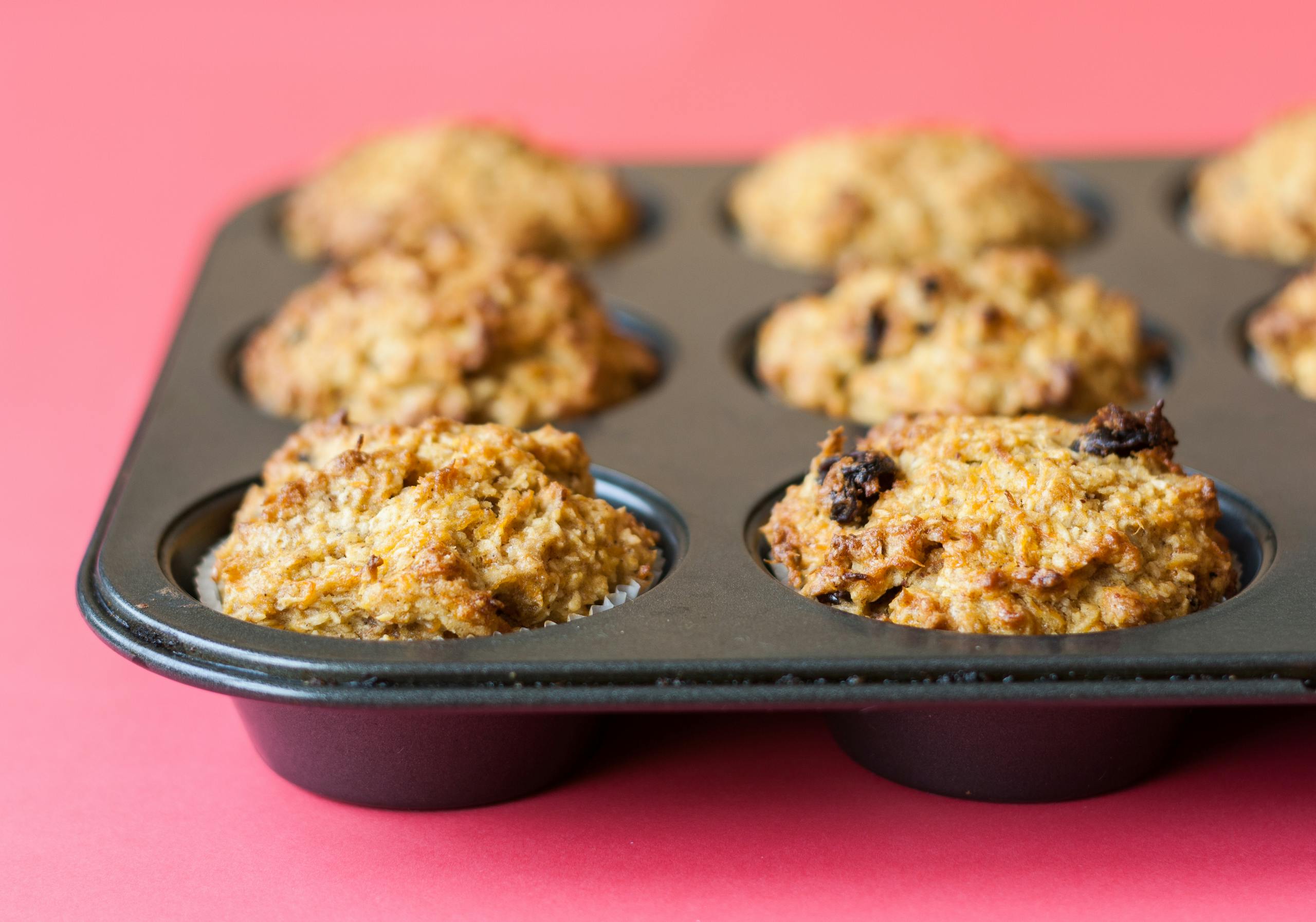 Delicious homemade muffins in a baking tray on a vibrant pink backdrop.