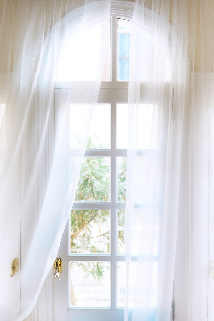 Spacious light house with white entrance door with windows and golden handle located under transparent curtains in daylight