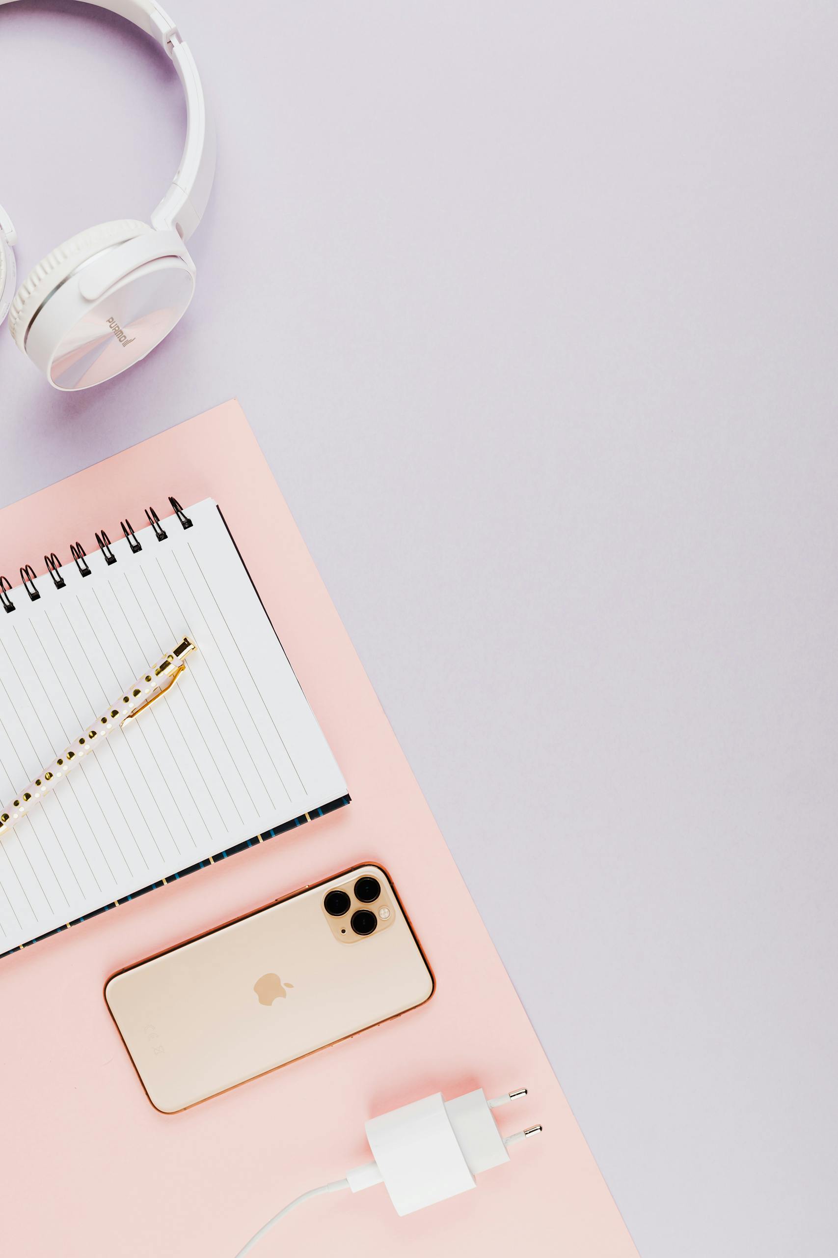 Stylish flat lay of smartphone, headphones, and notebook on pastel surface for modern tech themes.