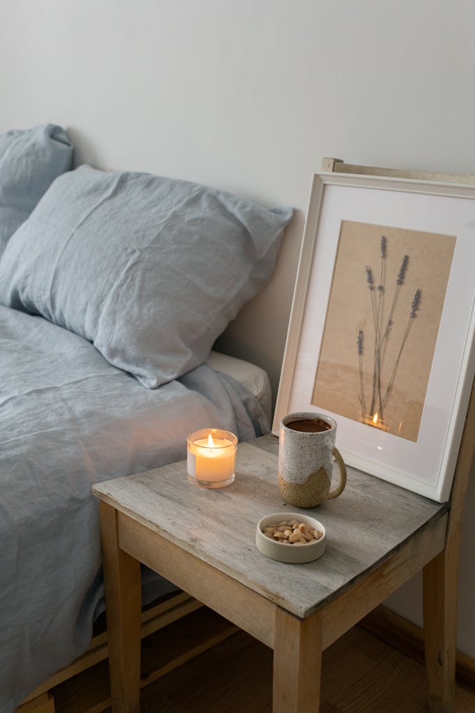 A serene bedroom scene with a lit candle, framed art, and cozy linens on a wooden nightstand.