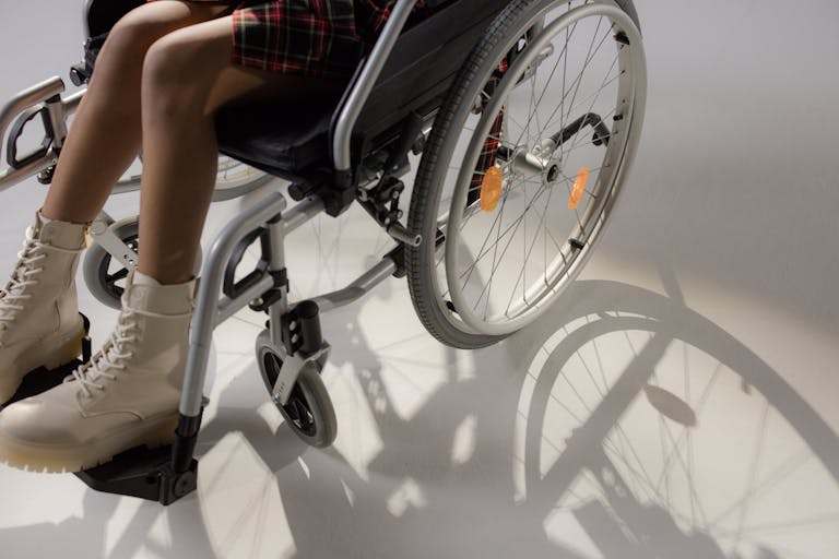 A young woman sitting in a wheelchair, wearing stylish beige boots, casting a shadow.