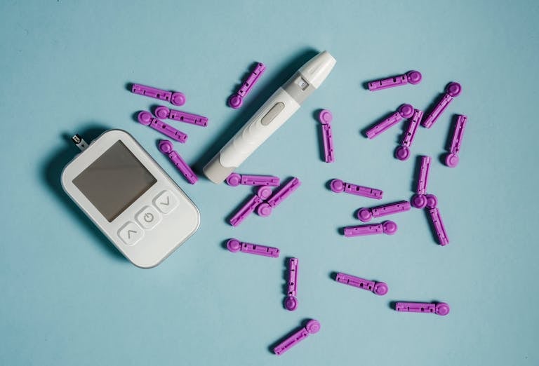 Top view of lancets scattered around blood glucose meter and lancing device on blue background