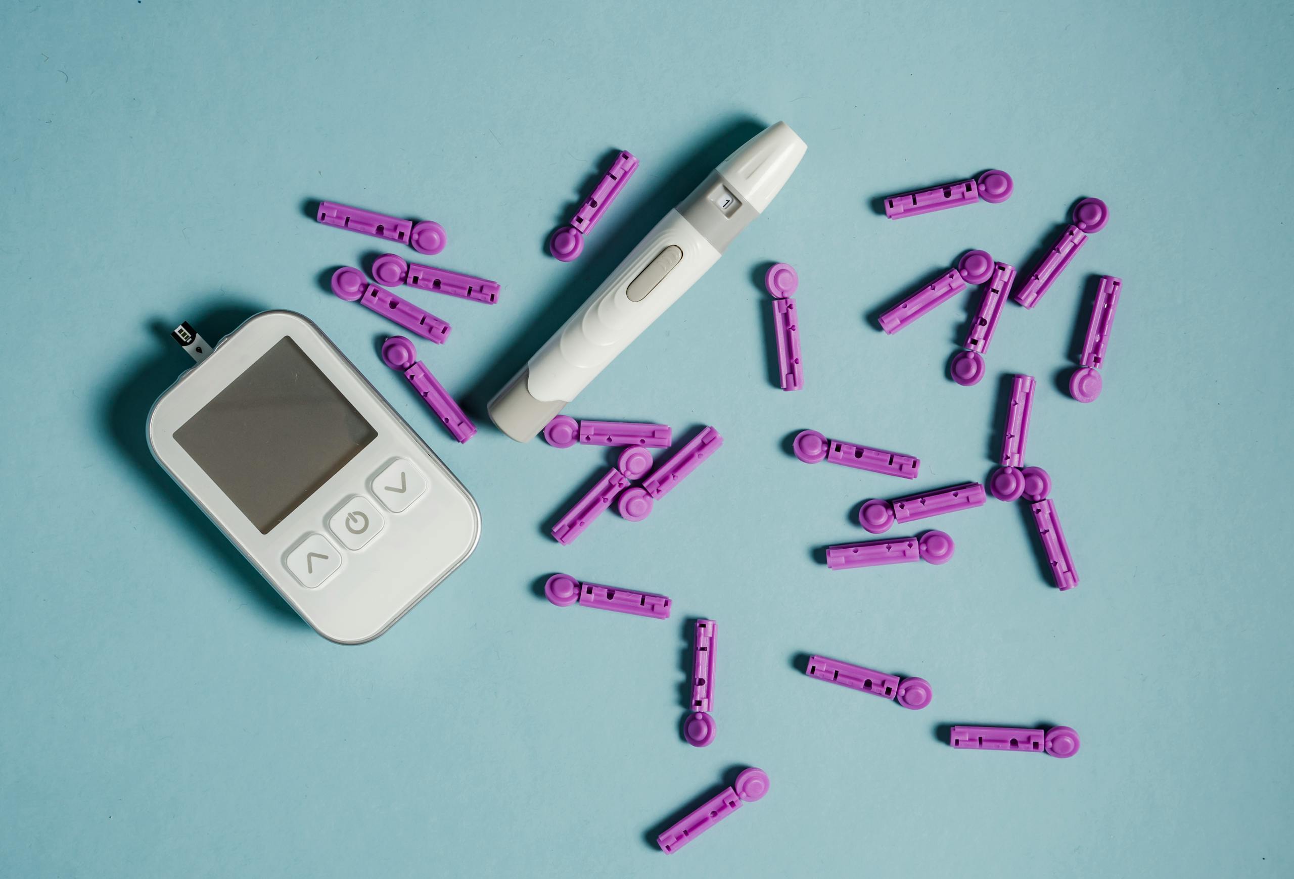 Top view of lancets scattered around blood glucose meter and lancing device on blue background