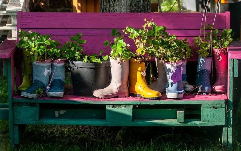 Vibrant rain boots repurposed as planters with lush greenery on a painted garden bench.