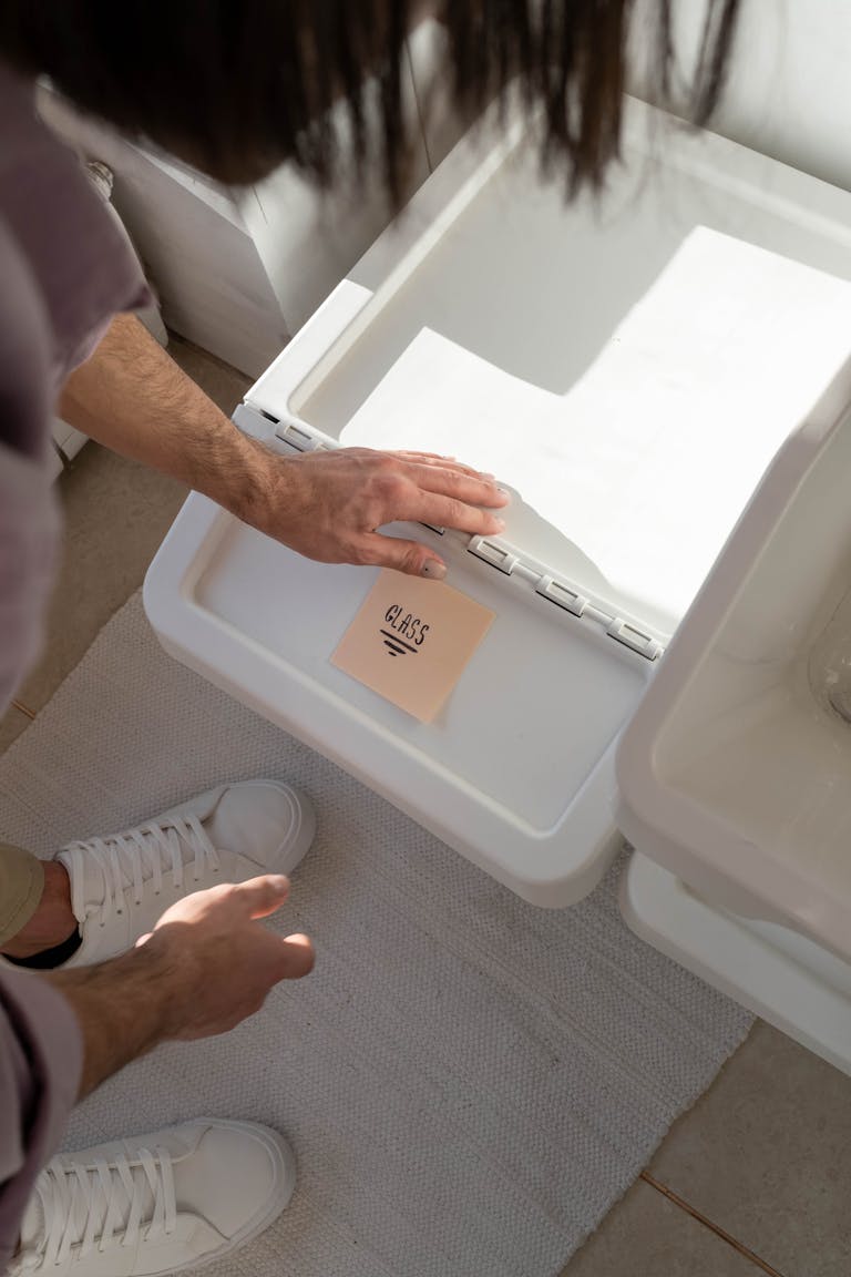 An adult man sorting glass waste in the kitchen for recycling, promoting eco-friendly practices.